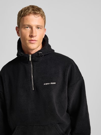 Männermodel trägt schwarzen Fleecepullover mit Reißverschluss Modell 'Olten' von Pegador, Kapuze, Känguru-Tasche, Nahaufnahme Oberkörper.