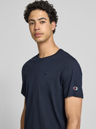Männermodel trägt T-Shirt mit Label-Stitchings und Rundhalsausschnitt von CHAMPION in Dunkelblau, Reine Baumwolle, Regular-Fit, Nahaufnahme Oberkörper.