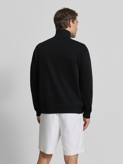 Männermodel trägt Regular Fit Troyer aus reiner Baumwolle von Lacoste in Schwarz, weiße Shorts, Ganzkörperansicht Rückansicht. Herren Troyer von Lacoste.