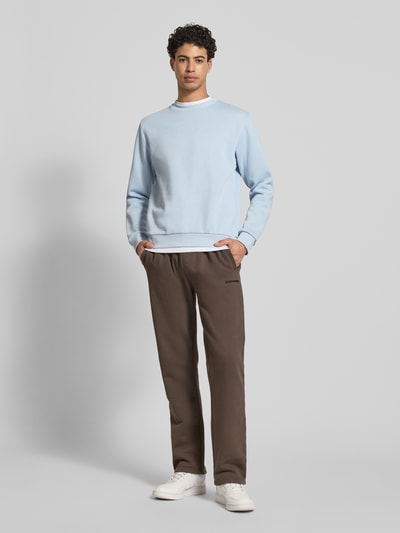 Męskimodel nosi bluza Sweatshirt mit gerippten Abschlüssen Modell 'BRADLEY' od JACK & JONES, mieszanka bawełny, krój regular fit, okrągły dekolt, prążkowane wykończenia, pastelowy niebieski, brązowe spodnie, długość tyłu w rozmiarze M: 67 cm, długość rękawów: 65 cm, pełen widok z przodu.