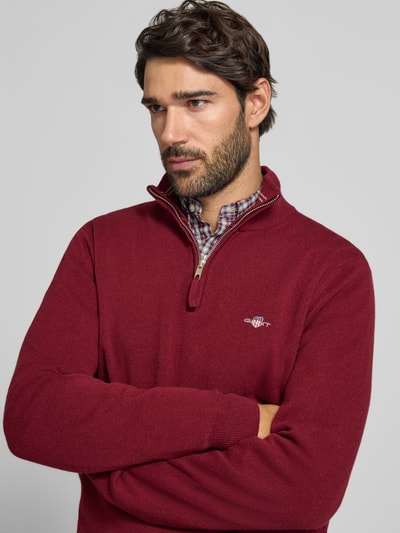 Männermodel trägt Pullover aus reiner Wolle von GANT in Dunkelrot, Feinstrick, hochgeschlossener Troyerkragen, Nahaufnahme Oberkörper.