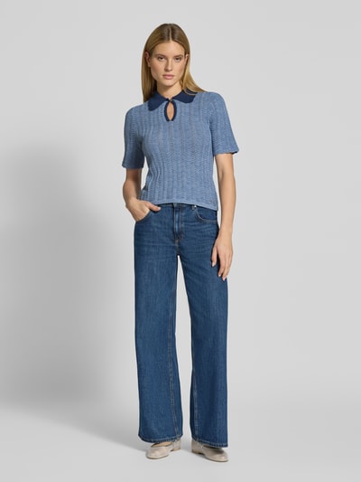 Frauenmodel trägt Strickshirt mit Umlegekragen und Schlüsselloch-Ausschnitt von Scotch & Soda, Slim Fit, Kurzarm, Baumwoll-Mix, blaue Töne, lockere Jeans, ruhiger Hintergrund, Ganzkörperansicht von vorne.