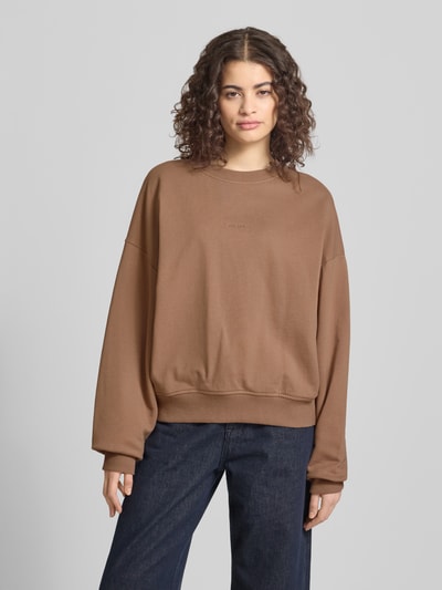 Frauenmodel trägt Regular Fit Sweater mit Logo-Stitching Modell 'Croissant' von OH APRIL in Braun aus reiner Baumwolle, Rundhalsausschnitt, elastische Abschlüsse, Ganzkörperansicht von vorne.