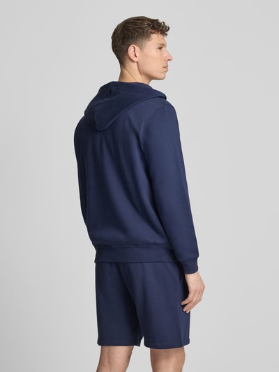 Männermodel trägt Sweatjacke mit Logo und Känguru-Tasche von GAP aus Baumwoll-Mix, Regular-Fit, Kapuze, Reißverschluss, Rückenlänge 70 cm, Ärmellänge 67 cm, dunkles Blau, glatte Textur, Ganzkörperansicht Rückansicht.