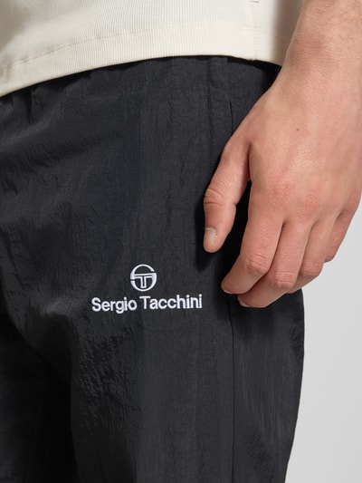 Männermodel trägt Straight Fit Stoffhose mit Logo-Stitching Modell 'Nayla' von SERGIO TACCHINI in Schwarz mit Struktur, Nahaufnahme Oberschenkel. Herren Stoffhose, elastischer Bund mit Tunnelzug, elastische Beinabschlüsse, Innenbeinlänge bei Größe M: 77 cm.