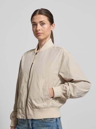 Modelka kobieca nosi Regular Fit Jacke mit Stehkragen od camel active w beżowym kolorze, elastyczne wykończenia, kieszenie, zamek dwukierunkowy, długość tyłu w rozmiarze 36: 55 cm, szerokość ramion: 43 cm, szerokość klatki piersiowej: 53 cm, długość rękawa: 59 cm, widok całej sylwetki z przodu
