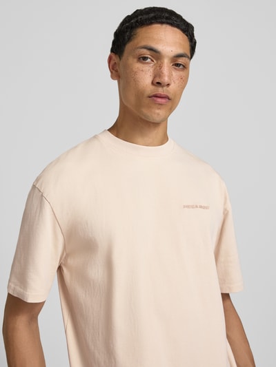 Männermodel trägt Oversized T-Shirt mit Label-Stitching von Pegador, Baumwoll-Mix, Rundhalsausschnitt, beige, Nahaufnahme Oberkörper. Herren T-Shirt, Rückenlänge bei Größe M: 70 cm.