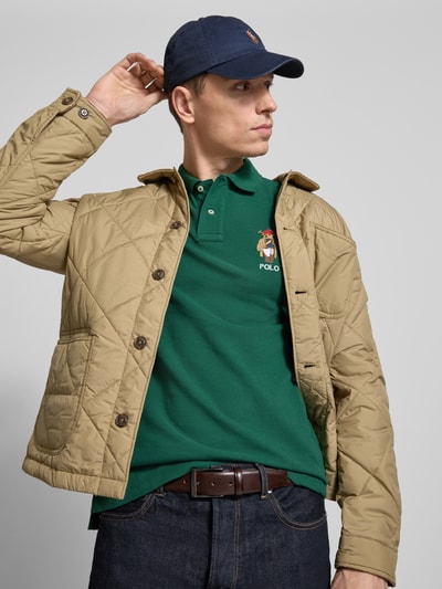 Mężczyzna nosi Regular Fit Poloshirt aus reiner Baumwolle von Polo Ralph Lauren, jednolity kolor, wyhaftowany motyw, zielony, pika, bawełna, krój regular fit, kołnierzyk polo, dekolt w serek, krótka listwa guzikowa, krótki rękaw, prążkowane zakończenie rękawów, rozcięcia po bokach, asymetryczny dół, widok na górną część ciała z przodu.
