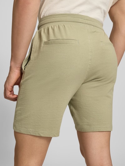 Männermodel trägt Loose Fit Sweatshorts aus Bio-Baumwoll-Mix Modell 'KIAN' von Only & Sons, grün, Piqué-Struktur, Ganzkörperansicht Rückansicht.
