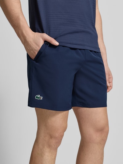 Männermodel trägt Loose Fit Sport-Shorts mit Mesh-Bund von Lacoste Sport in Unifarben mit Logo-Stitching und seitlichen Taschen, Nahaufnahme Oberschenkel.