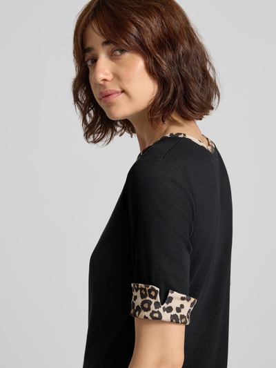 Frauenmodel trägt Regular Fit T-Shirt mit Animal-Print von Marc Cain aus elastischem Baumwoll-Mix, Schwarz mit Leopardenmuster-Details, Nahaufnahme Oberkörper.