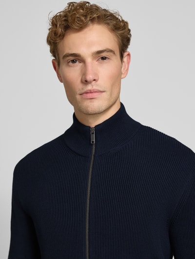 Männermodel trägt Strickjacke mit Stehkragen Modell 'LEVI' von MCNEAL in Dunkelblau, feine Rippenstruktur, Nahaufnahme Oberkörper, Baumwoll-Mix, gerader Schnitt.