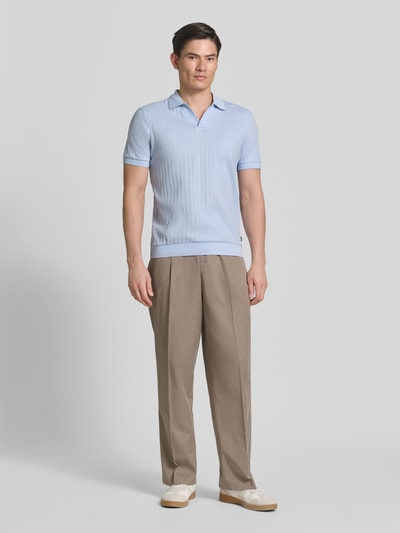 Männermodel trägt Regular Fit Poloshirt mit V-Ausschnitt Modell 'Baronito' von JOOP! Collection aus reiner Baumwolle mit Strukturmuster in Hellblau, kombiniert mit beigefarbener Hose und weißen Schuhen, Ganzkörperansicht von vorne.