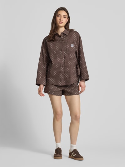 Frauenmodel trägt Relaxed Fit Bluse im Allover-Look Modell 'FRIDA' von Noisy May im Material-Mix mit Baumwoll-Anteil, Hemdblusenkragen, Brusttasche und Label-Detail, braun mit weißen Punkten, Ganzkörperansicht von vorne.
