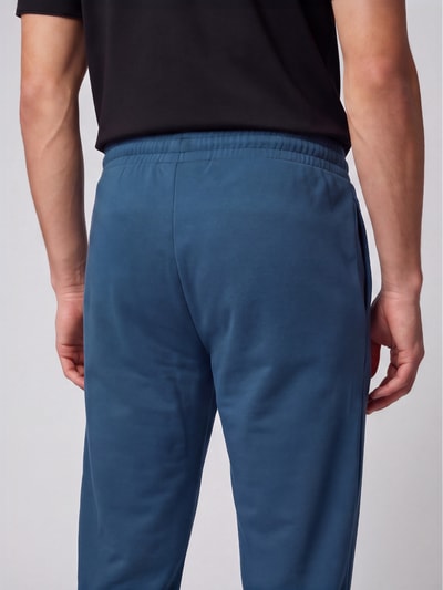 Männermodel trägt blaue Hose mit glatter Oberfläche, elastischem Bund und seitlichen Nähten, Nahaufnahme Rückansicht.