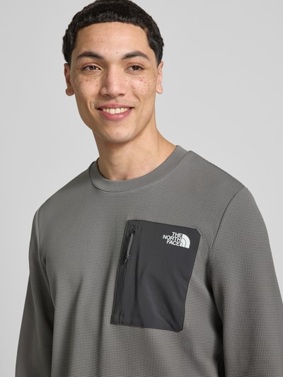 Männermodel trägt Langarmshirt mit Napoleontasche Modell 'KECHA' von The North Face, Elastischer-Material-Mix, Label-Detail, Nahaufnahme Oberkörper.
