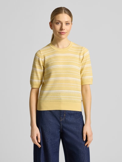 Vrouwenmodel draagt gebreide pullover uit katoenmix van Scotch & Soda in geel met getailleerde pasvorm, ronde hals, tricotlook, 3/4-mouw, ruglengte maat S 52 cm, mouwlengte maat S 30 cm. Ganzkörperaanzicht van voren.