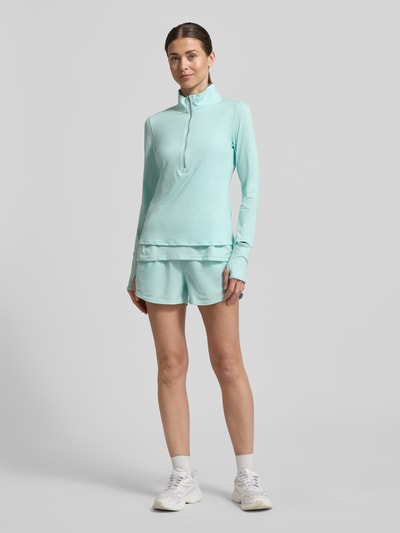Frauenmodel trägt Longsleeve mit Stehkragen und Reißverschluss von Under Armour aus Material-Mix mit Stretch-Anteil, Regular-Fit, Logo, Rückenlänge bei Größe S: 59 cm, hellblau, Ganzkörperansicht von vorne.