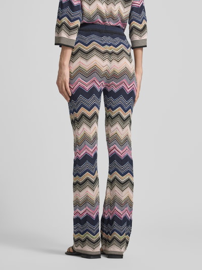 Frauenmodel trägt Flared Hose aus Viskose-Mix im Allover-Look von Oui mit Zickzack-Muster in Blau, Beige, Rosa, elastischer Bund, Ganzkörperansicht Rückansicht.