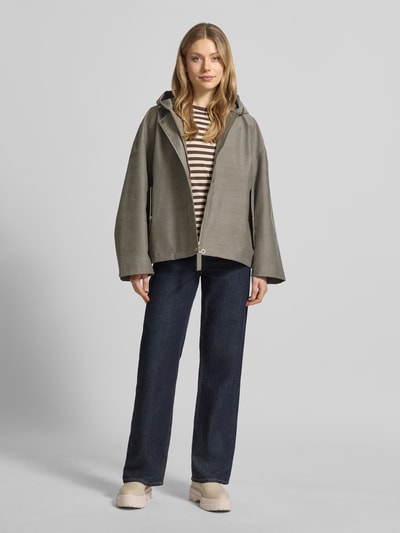 Frauenmodel trägt Regular Fit Jacke mit Kapuze Modell 'Elle' von G-LAB, Eingrifftaschen mit Druckknopfverschluss, Tunnelzug, olive, glatte Textur, Ganzkörperansicht von vorne. Rückenlänge bei Größe S: 64 cm, Schulterbreite: 56 cm, Brustweite: 56 cm, Ärmellänge: 51 cm.