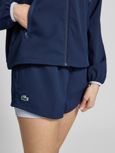 Frauenmodel trägt Regular Fit Sport-Shorts mit Logo-Applikation von Lacoste Sport in Unifarben Dunkelblau, elastischer Bund, Piqué-Stretch-Material, Nahaufnahme Oberschenkel.