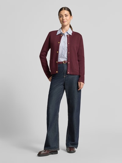 Frauenmodel trägt Regular Fit Strickjacke aus reiner Baumwolle von GANT in Dunkelrot, kombiniert mit blauer Jeans, Ganzkörperansicht von vorne. Damen Strickjacke von GANT.