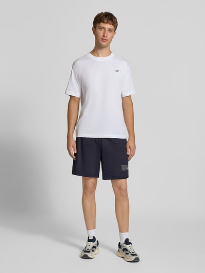 Männermodel trägt Sweatshorts aus Baumwoll-Mix von New Balance in Dunkelblau, gerader Schnitt, elastischer Bund, Label-Print, Ganzkörperansicht von vorne.