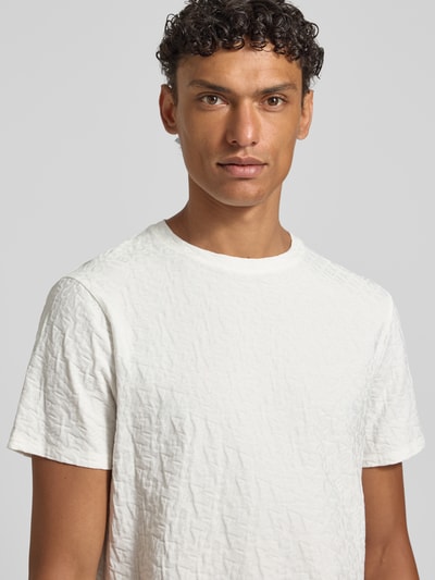Męski model nosi T-Shirt mit Logo-Muster und Rundhalsausschnitt od ARMANI EXCHANGE, biała bawełna, krój slim fit, logo, ujęcie z przodu, zbliżenie na górną część ciała.