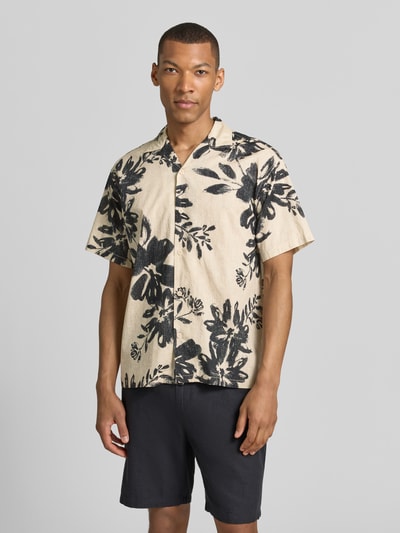 Männermodel trägt Relaxed Fit Freizeithemd mit Reverskragen Modell 'BLAVENICE' von Jack & Jones Premium, florales Muster, Vorderansicht Ganzkörperansicht. Bio-Baumwoll-Mix, Knopfleiste, beige Grundfarbe mit schwarzen Akzenten.