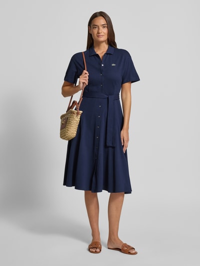 Frauenmodel trägt Tailliertes Freizeitkleid aus reiner Baumwolle von Lacoste in Unifarben Navy mit Label Patch, Midi-Länge, Ganzkörperansicht von vorne.