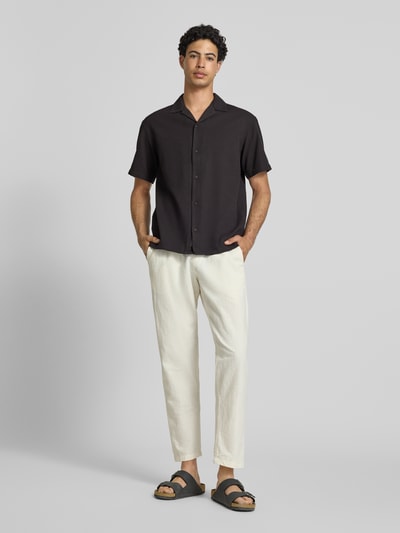 Männermodel trägt Regular Fit Freizeithemd mit Strukturmuster Modell 'Global' von Jack & Jones aus reiner Baumwolle, schwarz, Reverskragen, durchgängige Knopfleiste, kurzärmelig, Ganzkörperansicht von vorne.