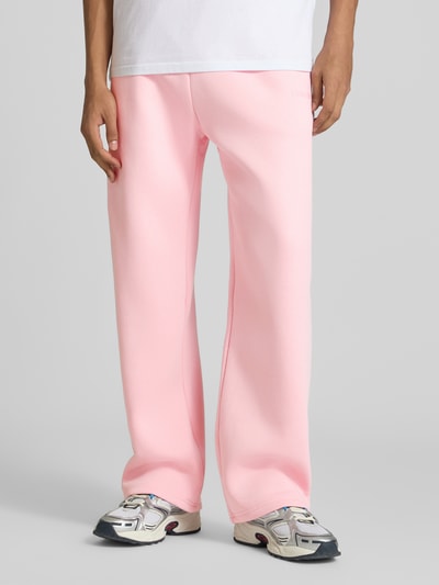 Männermodel trägt Straight Fit Sweatpants Baumwoll-Mix von REVIEW in Hellrosa mit Gesäßtasche, Tunnelzugbund, seitlichen Eingrifftaschen, Label-Print, Ganzkörperansicht von vorne.