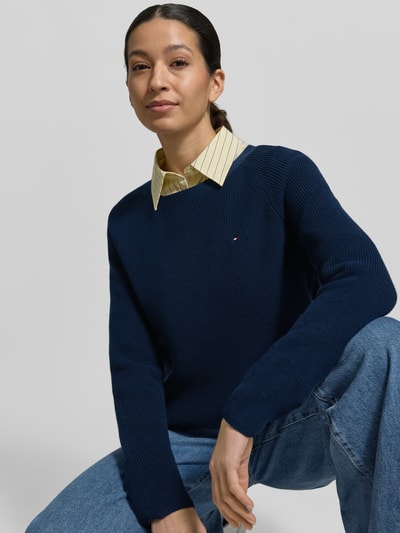 Vrouwenmodel draagt Regular Fit Pullover uit puur katoen van Tommy Hilfiger in effen donkerblauw met logostitching en ribtricot, close-up bovenlichaam.