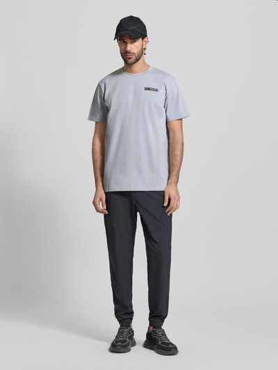 Męski model nosi Regular Fit T-Shirt mit Logo-Applikation od Under Armour z bawełnianej mieszanki, jasnoszary, dekolt okrągły, długość tyłu w rozmiarze M: 73 cm, krój regular fit, widok całej sylwetki z przodu.