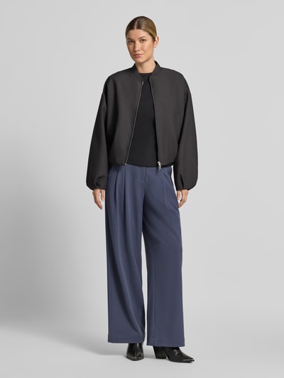 Frauenmodel trägt High Waist Bundfaltenhose mit Bügelfalten Modell 'Henrika' von MSCH COPENHAGEN in uni-blauem Viskosemix mit Bundfalte, Gürtelschlaufen und seitlichen Eingrifftaschen, Ganzkörperansicht von vorne.