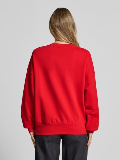 Frauenmodel trägt Oversized Sweatshirt aus reiner Baumwolle Modell 'ICONIC A ALIZAA' von Armedangels, einfarbig rot, Sweat-Textur, gerippte Abschlüsse, Logo-Stitching dezent, Ganzkörperansicht Rückansicht.