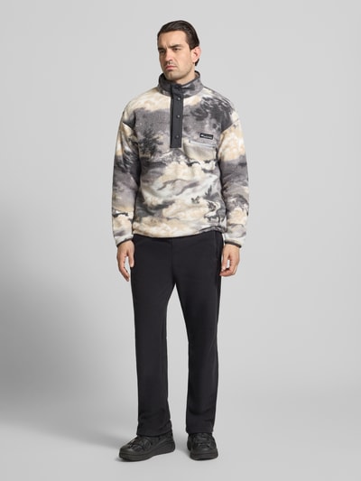 Męski model nosi Regular Fit Pullover mit Logo-Patch od Columbia o fließ-Optik, kieszeń na piersi, stójka z listwą z zatrzaskami, elastyczne wykończenia, długość tyłu 72 cm, długość rękawów 49 cm, widok całej sylwetki z przodu.