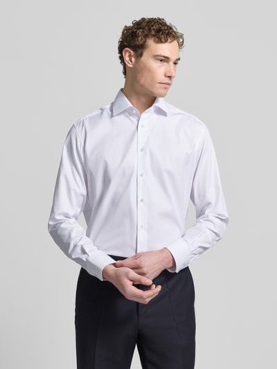 Männermodel trägt Regular Fit Businesshemd aus Uni Solid von ETERNA in Weiß, Reine Baumwolle, Kentkragen, Knopfleiste, Sportmanschetten, Brusttasche, Kontrastausputz, Bügelleicht, Blickdicht, Bügelfrei, Made in Europe, Ganzkörperansicht von vorne.