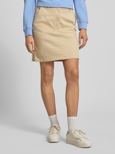 Kobiece model prezentuje Minirock mit Gesäßtaschen od Gant, beżowy bawełniano-elastanowy, prosty krój, kieszenie z tyłu, szerokość w rozmiarze 36: 39 cm, długość całkowita 47 cm. Ujęcie: całe ciało z przodu.