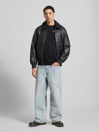 Männermodel trägt Regular Fit T-Shirt mit Logo-Print von Calvin Klein Jeans in Schwarz, reine Baumwolle, Rundhalsausschnitt, Ganzkörperansicht von vorne.