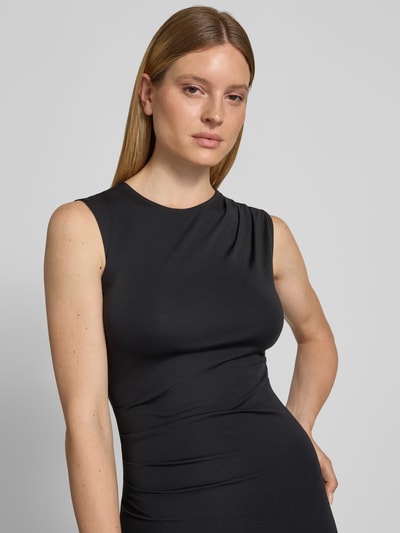 Modelka kobieca nosi sukienkę midi z mieszanki wiskozy z dodatkiem streczu od Jake*s Collection, podkreślająca figurę, okrągły dekolt, drapowania, szerokość w rozmiarze S: 38 cm, długość tyłu: 130 cm, kolor czarny, gładka tekstura, zbliżenie na górną część ciała, widok z przodu.