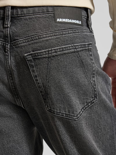 Männermodel trägt Tapered-Fit Jeans aus Bio-Baumwoll-Mix Modell 'MAAKX' von Armedangels in grauer Denim-Optik mit Label-Patch und 5-Pocket-Design, Detailaufnahme Rückansicht. Kontext: Herren Tapered-Fit Jeans Passform Relaxed Tapered-Fit, Bundhöhe Mid, Gürtelschlaufen, Knopf und verdeckter Reißverschluss, Material Bio-Baumwoll-Mix.
