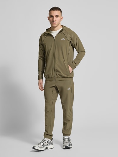 Männermodel trägt Regular Fit Trainingsjacke mit Kapuze von adidas Training in Optik: Unifarben, Ganzkörperansicht von vorne. Passform: Regular-Fit, Verschluss: Reißverschluss, Applikation: Label-Print, Kragenform: Stehkragen mit Kapuze und Tunnelzug, Ärmelform: Langarm, Ärmelabschluss und Rumpfabschluss: Elastisch, mit CLIMACOOL Technologie, und seitlichen Eingrifftaschen.
