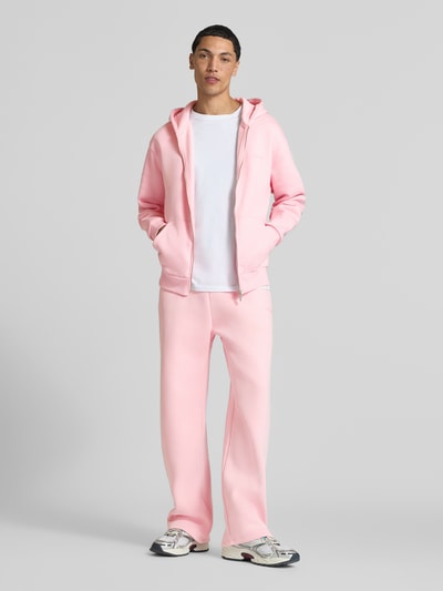 Männermodel trägt Straight Fit Sweatpants Baumwoll-Mix von REVIEW in Rosa mit Label-Print, Seitentaschen, Ganzkörperansicht von vorne.