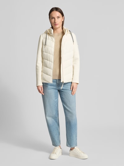 Modelka kobieca nosi Slim Fit Steppjacke mit gefüttertem Stehkragen od Christian Berg Woman Selection, kolor kremowy, krój slim fit, steppowana faktura, kaptur ze stójką, zamek błyskawiczny, kieszenie na zamek, długość tyłu w rozmiarze 36: 60 cm, szerokość ramion w rozmiarze 36: 41 cm, szerokość klatki piersiowej w rozmiarze 36: 51 cm, długość rękawa w rozmiarze 36: 62 cm, widok całej sylwetki z przodu.