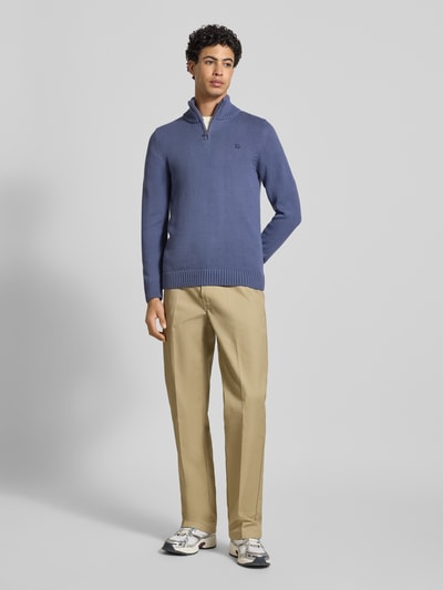 Männermodel trägt Slim Fit Pullover in Strick-Optik von Superdry in Blau mit Stehkragen, Reißverschluss und Logo-Stitching, Ganzkörperansicht von vorne. Rückenlänge 70 cm, Ärmellänge 65 cm bei Größe M.