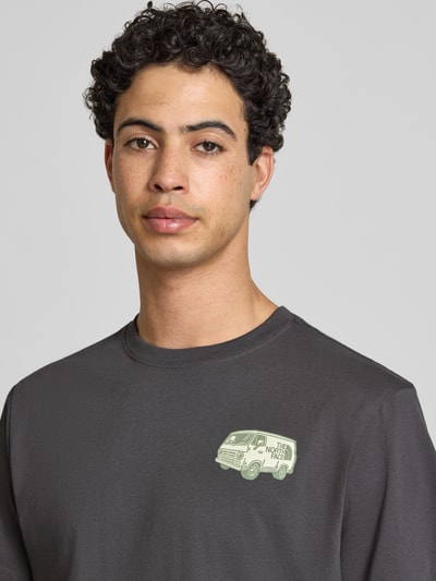 Männermodel trägt T-Shirt mit Label-Print und Rundhalsausschnitt von The North Face aus Baumwolle in Dunkelgrau, Nahaufnahme Oberkörper.