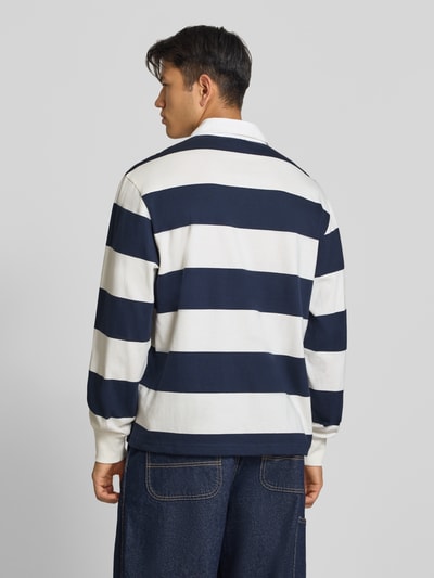 Männermodel trägt Relaxed Fit Poloshirt aus reiner Baumwolle von Champion, blau-weiße Blockstreifen, Statement-Stitching, Rückenansicht, Ganzkörperansicht Rückansicht, langärmeliges Design, Polokragen, Rückenlänge bei Größe M 71 cm