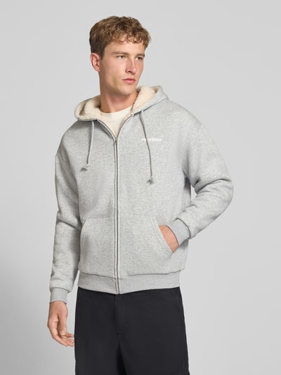 Männermodel trägt Regular Fit Sweatjacke aus Baumwoll-Mix mit Teddyfutter von REVIEW in Grau mit Känguru-Tasche, Ganzkörperansicht von vorne.