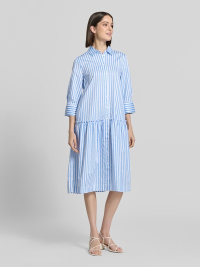 Frauenmodel trägt Relaxed Fit Hemdblusenkleid mit Rüschenbesatz von Christian Berg Woman aus Reine Baumwolle, blauer Streifenstoff, Hemdblusenkragen, 3/4-Arm, durchgängige Knopfleiste, Rückenlänge 109 cm, Brustweite 49 cm, Ärmellänge 48 cm, Ganzkörperansicht von vorne.